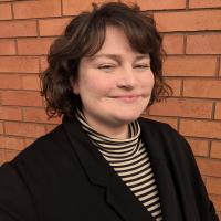 A photo of Kate Macdonald against a red brick background.